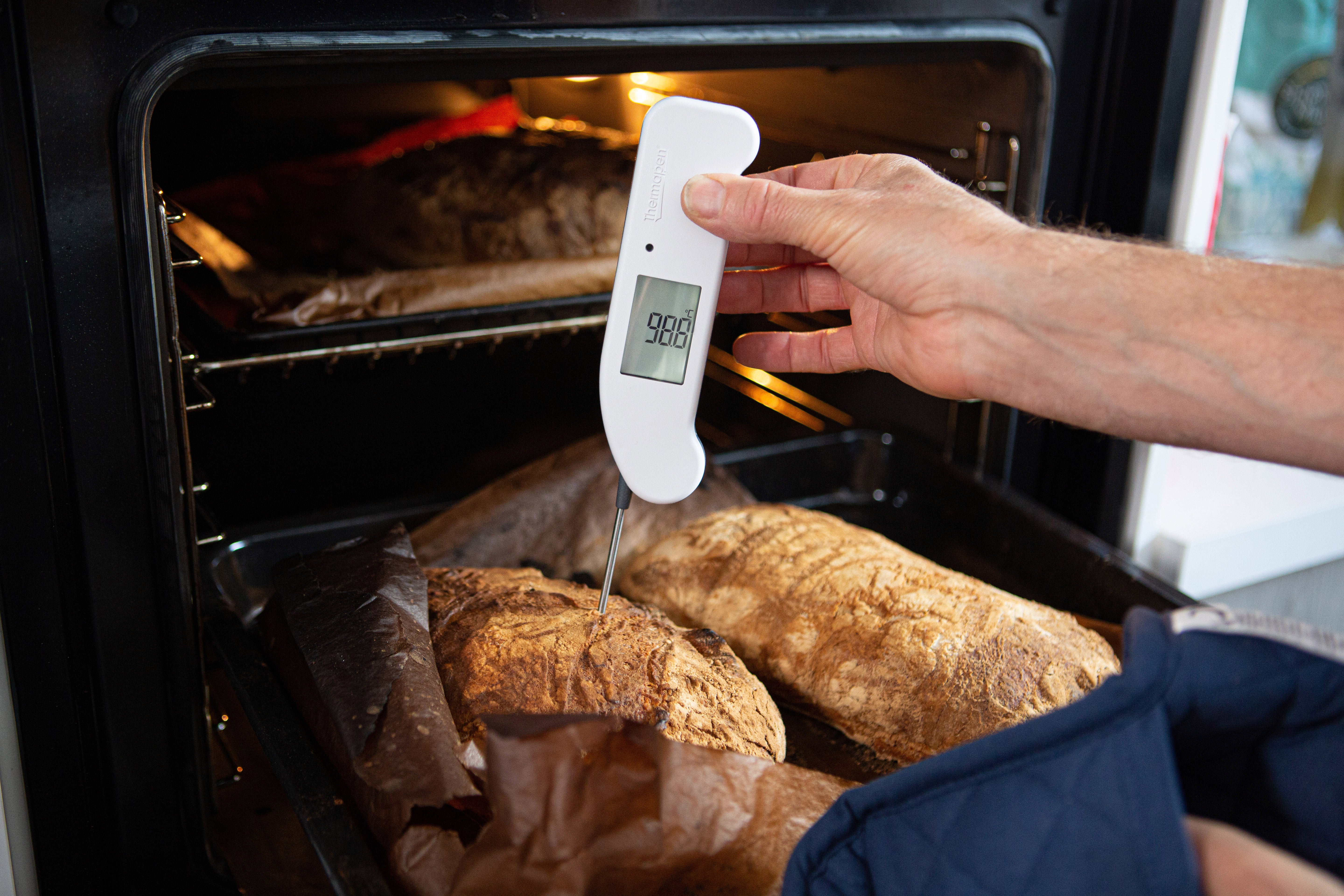 Thermapen One, weiß, gehalten in Hand, misst Kern-Temperatur von Brot in Backofen. Display zeigt 98,8 °C.