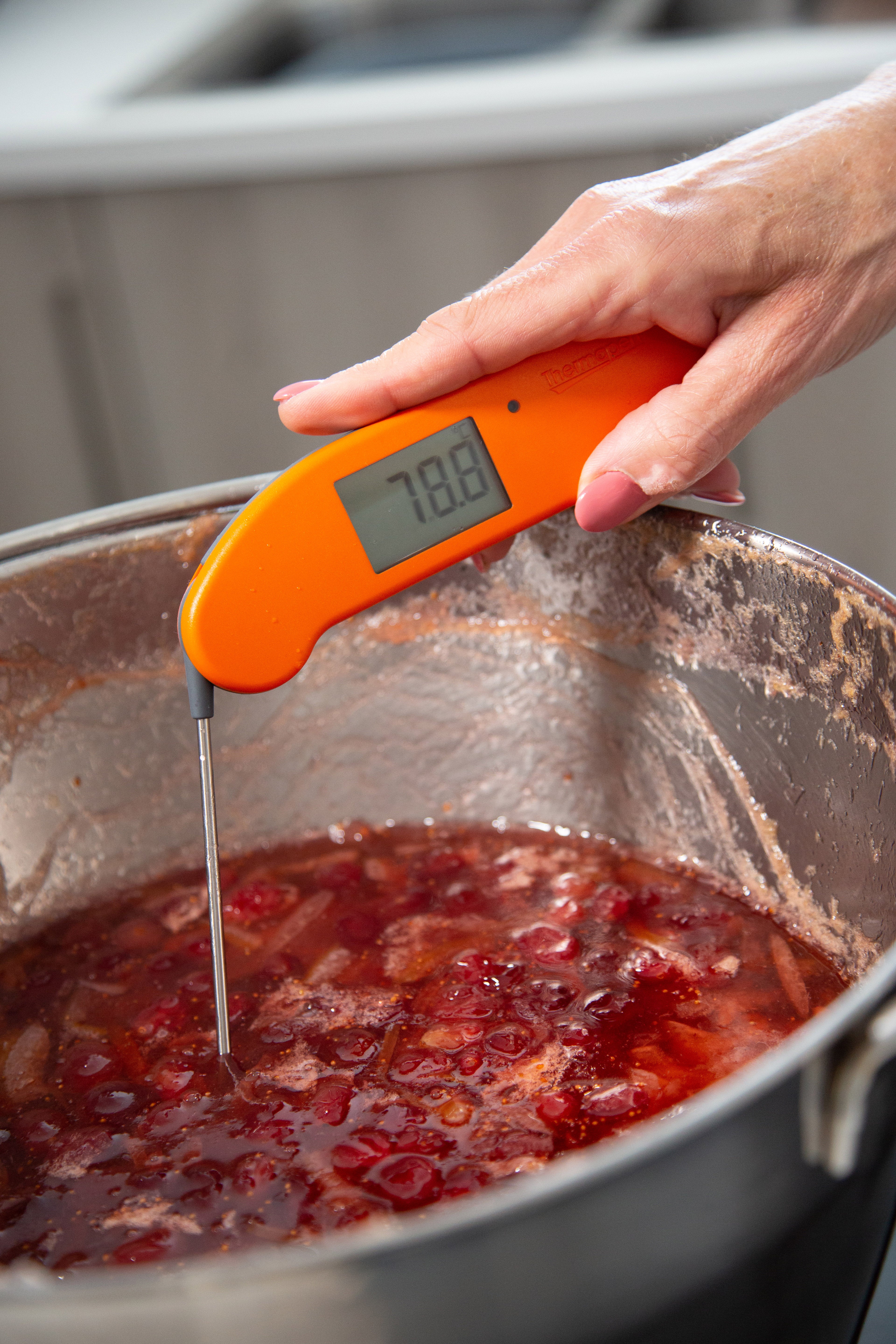 Thermapen One, orange, gehalten in Hand, misst Temperatur von Marmelade in Kochtopf. Display zeigt 78,8 °C.